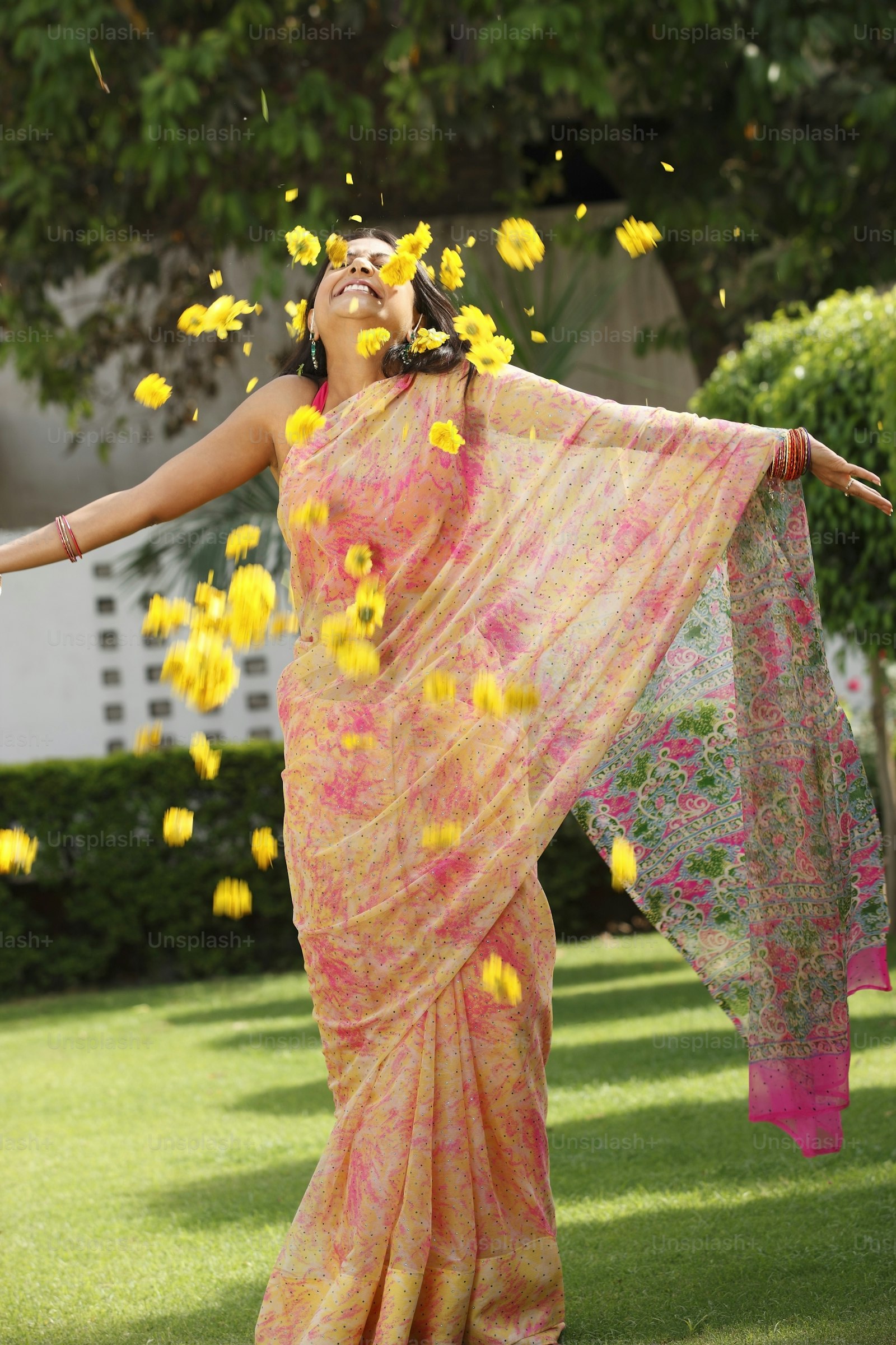 A woman in a handwoven silk saree with marigold petals caught mid-air, photographed in a temple garden