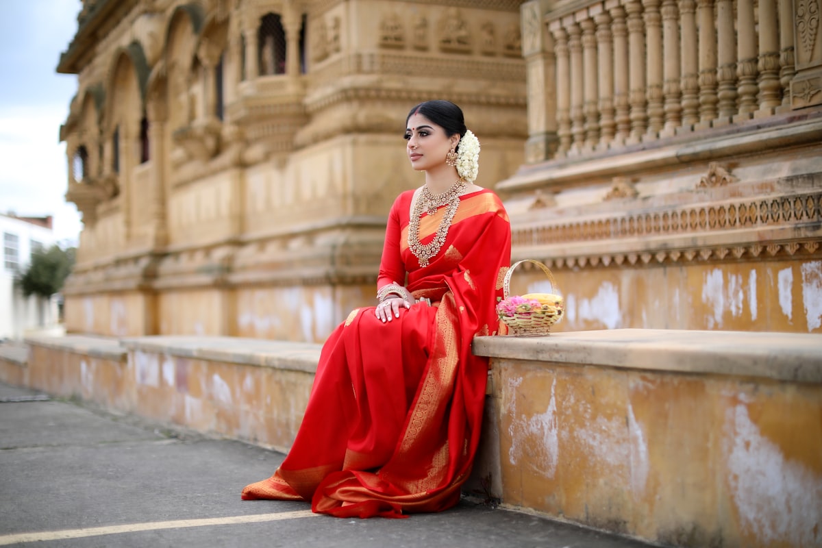 Deep plum Kanjivaram silk saree with gold zari border, photographed beside a temple wall
